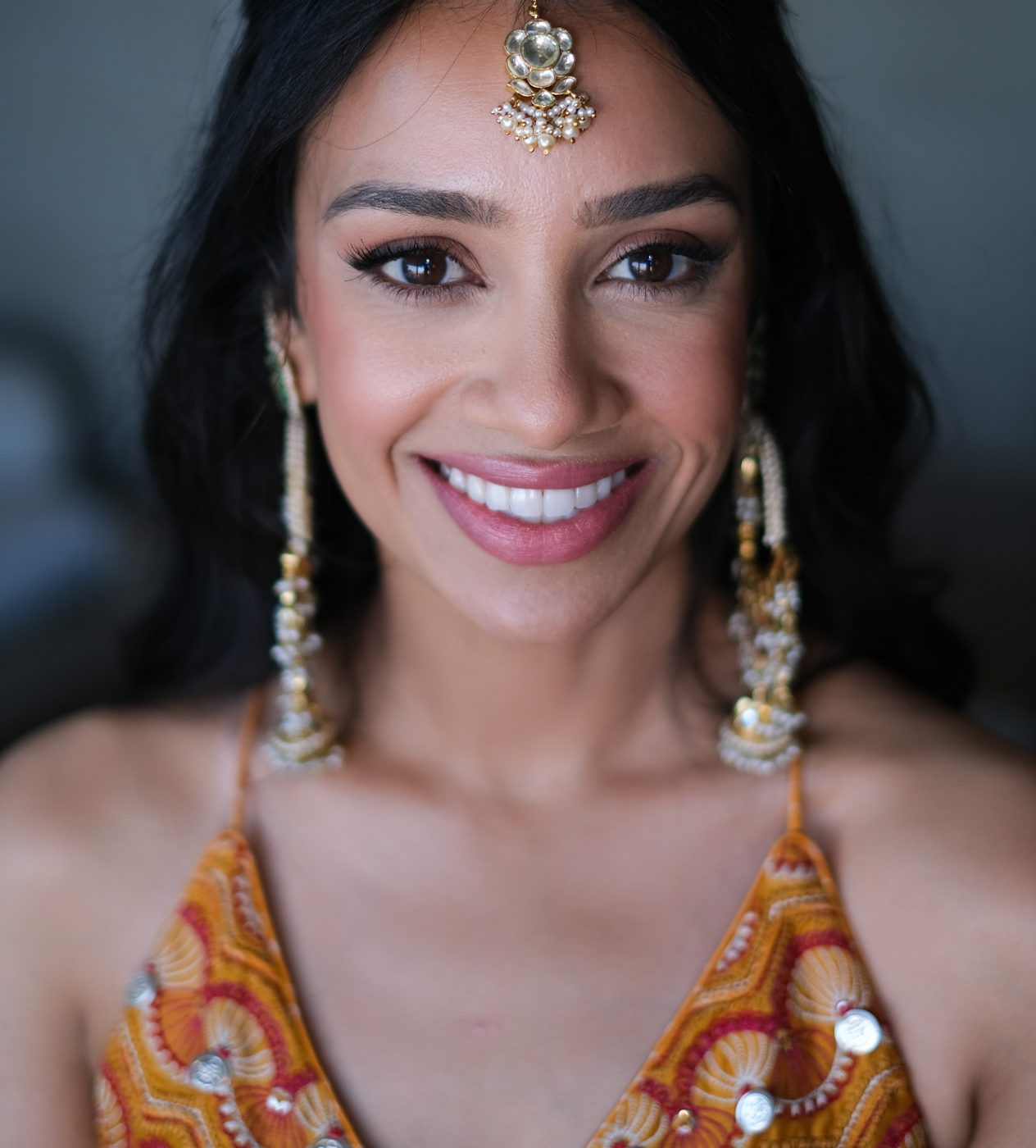 Smiling bride with maang tikka and gold jhumka earrings, festive glam